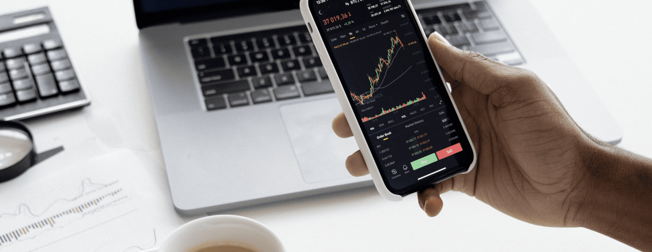 stock market on the laptop and on a mobile device and a cup of coffee and calculator next to them